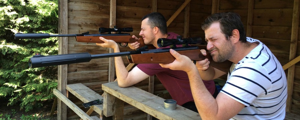 Two men alongside one another aiming rifles to shoot