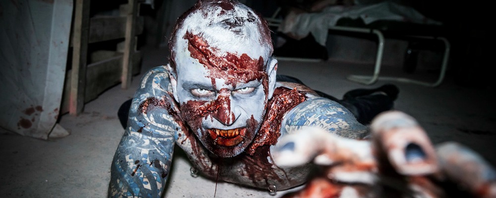 A zombie on the floor reaches towards the camera.