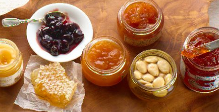 Jam, honey and other preserves on a wooden slab, photographed from above